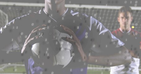 Holding goalkeeper wearing dark jersey clutching soccer ball at chest on night pitch, with goal net