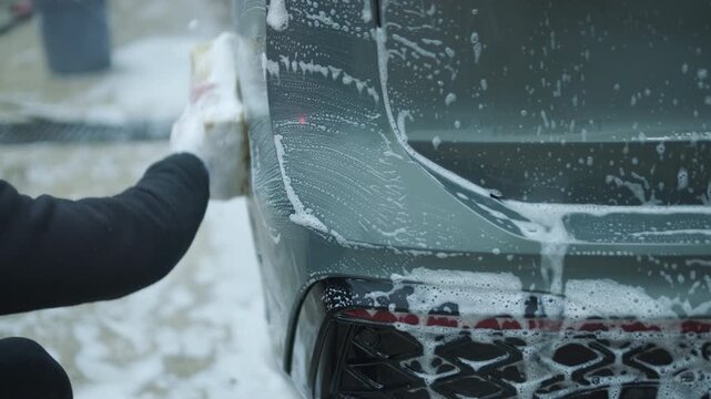 Сar wash worker cleaning vehicle windshield with soapy sponge. Man washing grey car with foam at the detailing garage.