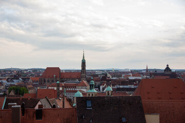 Obraz premium Panoramic view of a historic city skyline featuring red rooftops, church steeples, and cloudy skies, showcasing architectural diversity and urban landscape beauty