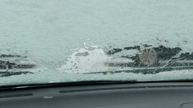 Wiper clearing ice patch on windshield leaving streaks and revealing partial view of wet road beyond