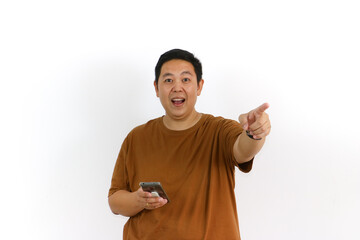Fototapeta premium An Asian male individual reacting with a winning gesture and excited facial expression while using a smartphone.