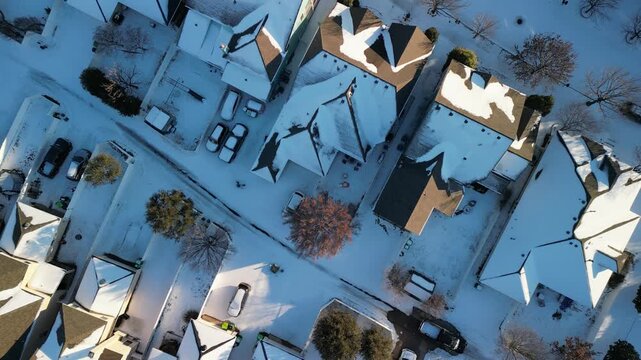 Drone aerial view of residential suburb with single-family homes covered in fresh snow on roofs, yards and streets under clear winter sky.