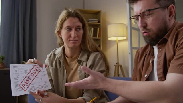 Tilt up shot of troubled adult couple holding bills with past due notice and discussing financial problems while doing budgeting together