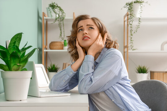 Young woman suffering from noisy neighbours near desk at home