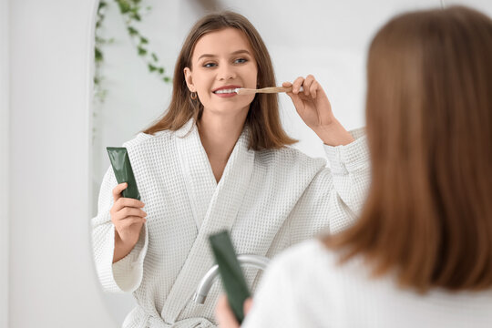 Young woman with dental braces cleaning teeth near mirror in bathroom