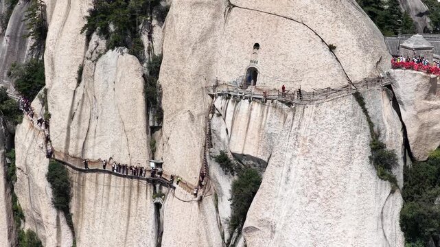 Aerial video close-up of the Longkong plank path at Mount Hua, narrow wooden walkway clinging to sheer cliffs, with hikers navigating the dramatic mountain route. China