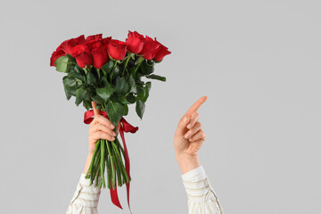 Female hands with bouquet of beautiful red rose flowers pointing at something on grey background