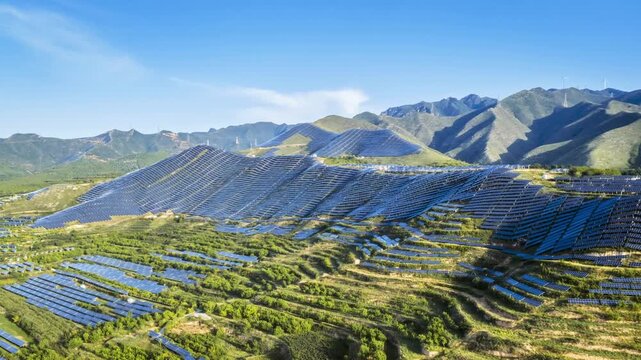 Aerial time-lapse of a mountain solar farm at early morning, with rows of photovoltaic panels stretching across rolling hills under clear blue sky.