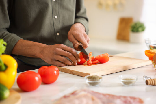Man cutting tomato at table in kitchen, closeup