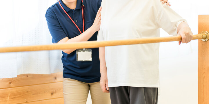 手すりを使い歩行訓練するシニア女性と介助する作業療法士,理学療法士の女性スタッフ