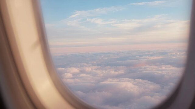 Soft pastel sunrise sky above fluffy cloud layer seen through airplane window, soft pastel clouds