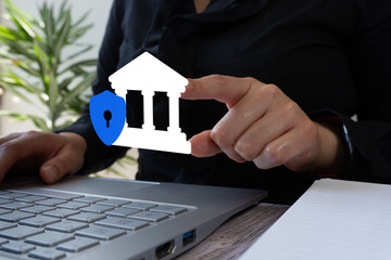 Businesswoman working on a computer, pointing at a bank icon with a shield. Cybersecurity concept in banking systems.	