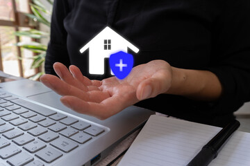 A woman discusses aspects of buying a house or insuring it. Abstract concept. A woman in front of a laptop with a floating icon of a house and a shield.