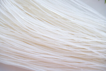 Obraz premium A textured macro shot of dry funchose or rice vermicelli. The thin, translucent white strands are tightly interwoven, creating an abstract linear pattern.