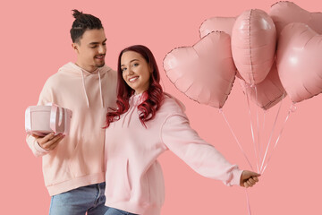 Young lovely couple with gift and heart-shaped balloons on pink background. Valentine's Day...