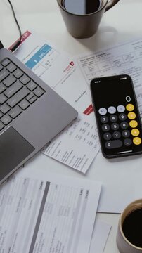 Vertical top view shot of scattered financial documents on coffee table with open computer and calculator