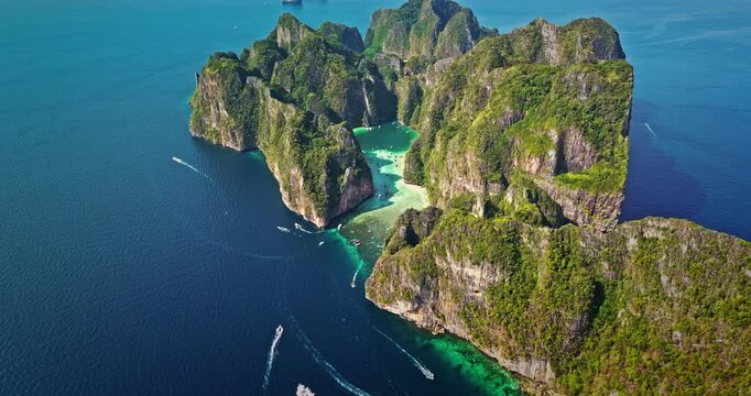 Aerial panorama of tropical Phi Phi Leh island with stunning limestone cliffs, lush green vegetation, and crystal clear turquoise waters in Maya Bay with longtail boats navigating the shallow lagoon
