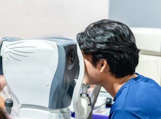 The patient is leaning forward with his head positioned against the medical device for a precise vision screening