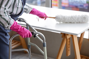 Woman with walker and pp-duster cleaning table at home