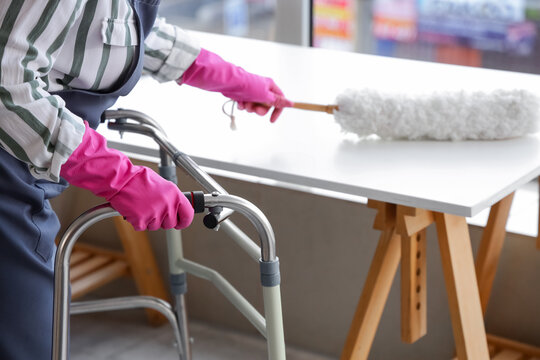Woman with walker and pp-duster cleaning table at home