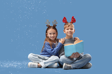 Naklejka premium Cute little children in Christmas reindeer horns with book and snow sitting on blue background