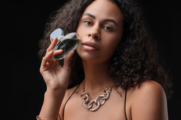 Obraz premium Pretty young African-American woman with bottle of perfume on black background