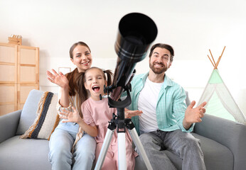 Fototapeta premium Little girl with her parents and telescope sitting on sofa at home