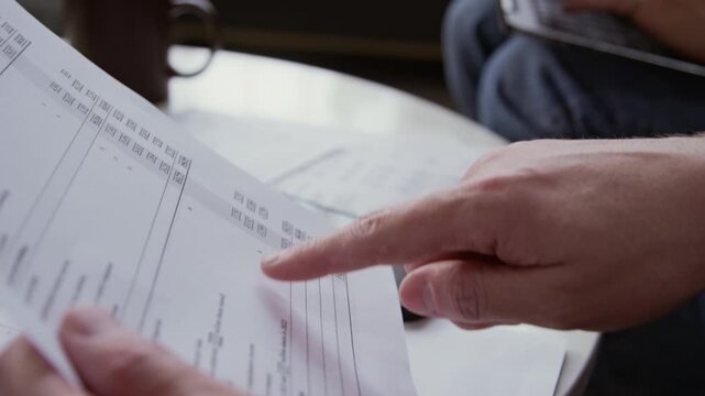 Side view close up shot of male hand pointing at banking balance sheet going down list of liabilities and assets making rational financial decisions, copy space