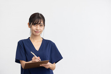 Obraz premium Smiling Young Asian Woman in Navy Medical Scrubs Holding Clipboard on White Background