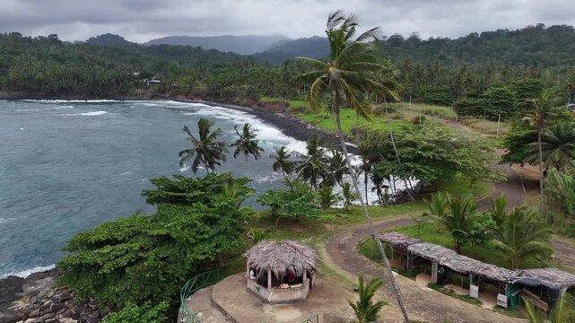 Aerial view of a scenic coastal road and lush hills in Sao Tome with palm tree beach and luxury eco village resort