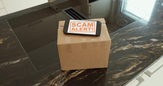 Close-up of a cardboard parcel on a kitchen countertop with a &ldquo;SCAM ALERT&rdquo; message displayed on a device above it. Perfect for themes like delivery scams, fake shipping notifications, online shopping