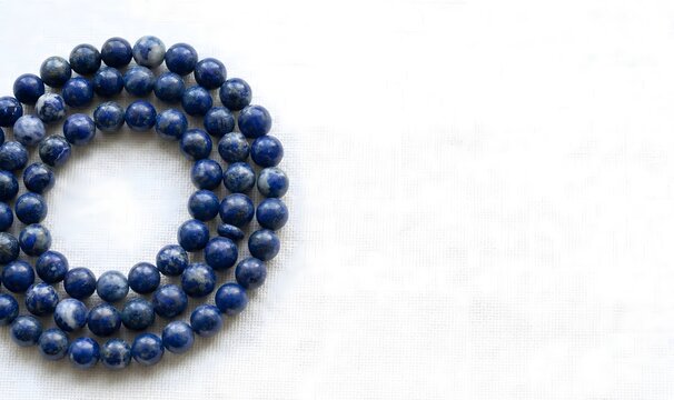 A coiled strand of natural blue gemstone beads, possibly lapis lazuli or sodalite, rests on a clean white textile background providing ample copy space.