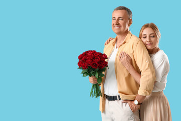 Happy mature couple with bouquet of roses on blue background. Valentine's Day celebration