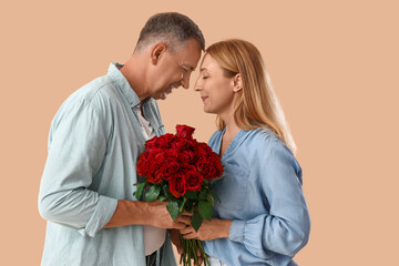 Happy mature couple with bouquet of roses on beige background. Valentine's Day celebration