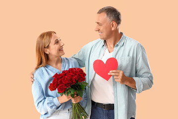 Happy mature couple with bouquet of roses and paper heart on beige background. Valentine's Day...