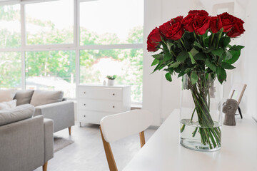 Vase with beautiful red roses on table in stylish living room