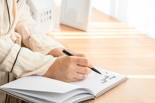 Young woman writing New Year goals at home, closeup