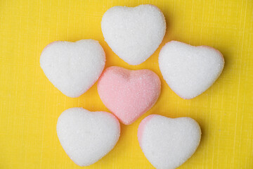 Fototapeta premium A creative arrangement of heart-shaped candies forming a flower shape, with a pink heart in the center surrounded by white hearts on a yellow textured background.