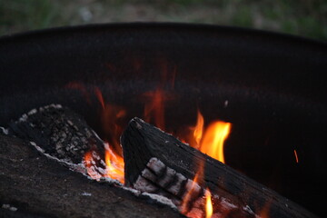 Orange Flames Rising From Charring Wood Logs In Dark Metal Fire Pit