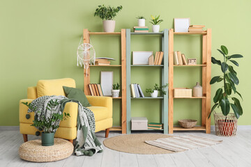 Comfortable armchair, pouf and book shelf near green wall in interior of living room © Pixel-Shot