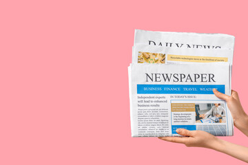 Female hands with newspapers on pink background
