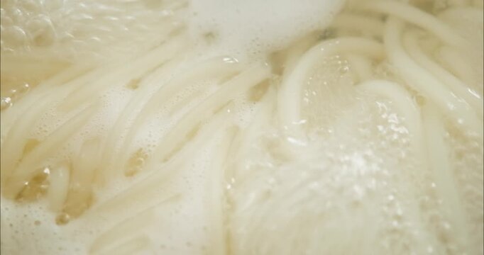 沸騰した鍋で煮て茹でる白いうどんのクローズアップ　和食・料理・調理　泡を立てて煮立つ暑い湯と湯気　