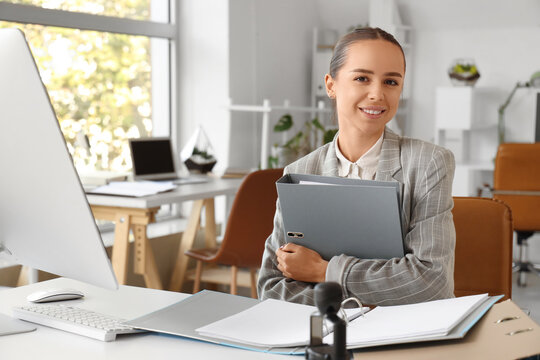 Young businesswoman with folder sitting at table in office