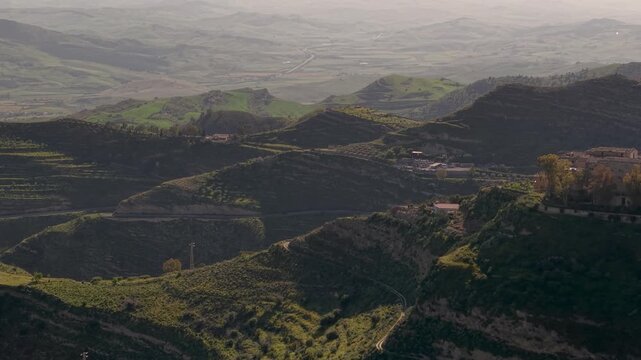 Aerial view over small terracotta properties on lush hazy Enna province mountain crest in Centuripe