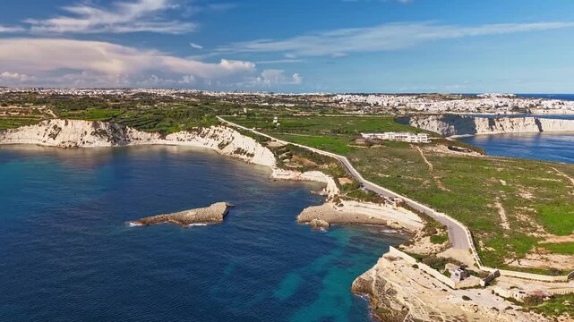 Aerial hyperlapse along Triq Xrobb L-Għaġin in southern Malta, revealing dramatic limestone cliffs, turquoise Mediterranean waters and a tranquil coastal landscape under a bright blue sky.