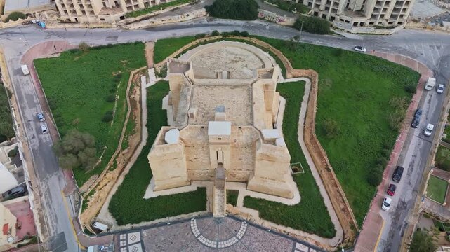 Descending aerial reveal view from the Torri San Tumas, a historic 17th-century watchtower, with the abandoned coastal Jerma hotel and the Mediterranean Sea in the background, in Marsaskala, Malta.