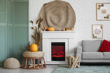 Naklejka premium Stylish living room with fireplace, comfortable sofa, coffee table and pumpkins. Autumn concept