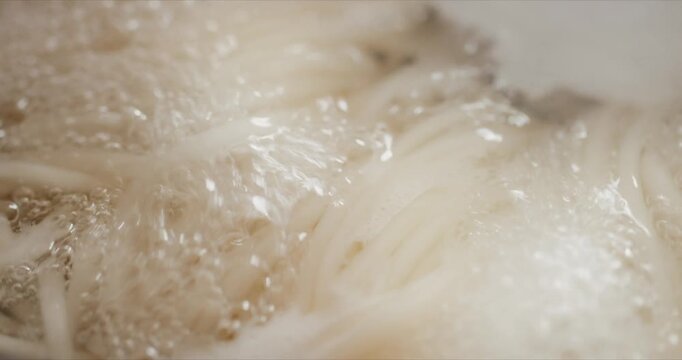 沸騰した鍋で煮て茹でる白いうどんのクローズアップ　和食・料理・調理　泡を立てて煮立つ暑い湯と湯気　