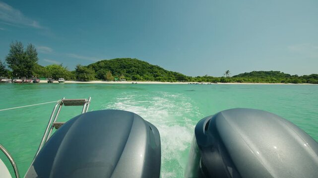 Speedboat leaving Pig Island with twin outboard engines, turquoise water and green tropical shoreline under clear blue sky in Thailand