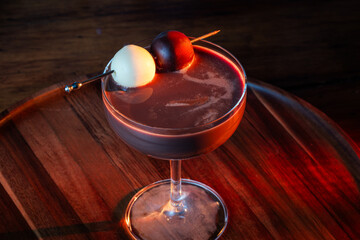 A rich chocolate dessert cocktail served in a coupe glass, featuring a dual garnish of dark and white chocolate truffles on a rustic wooden bar with warm, dramatic lighting.